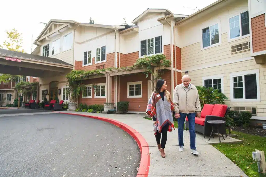 Senior man and caregiver walking outside assisted living home.