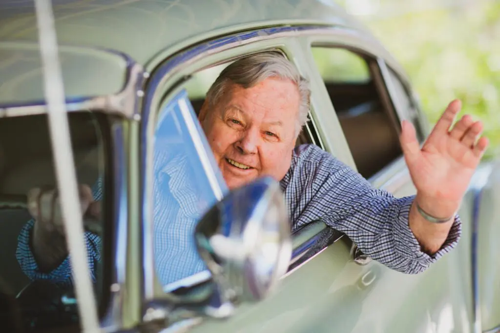 Smiling man waving from car window.