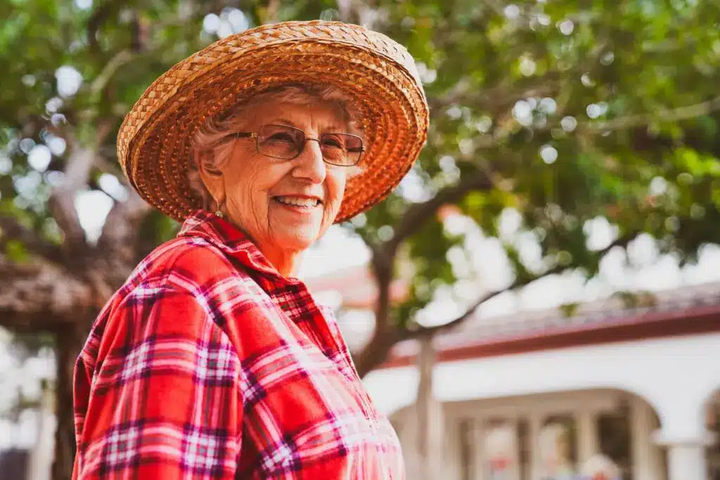 Elderly woman in plaid shirt and straw hat smiling.