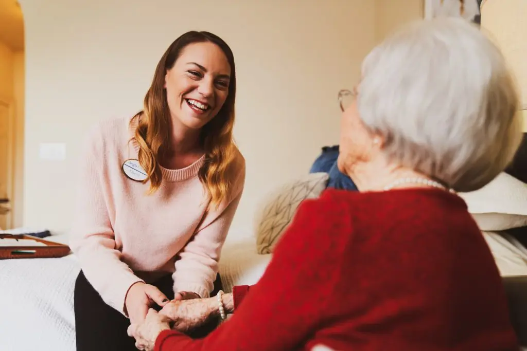 Caregiver smiling with elderly woman at home.