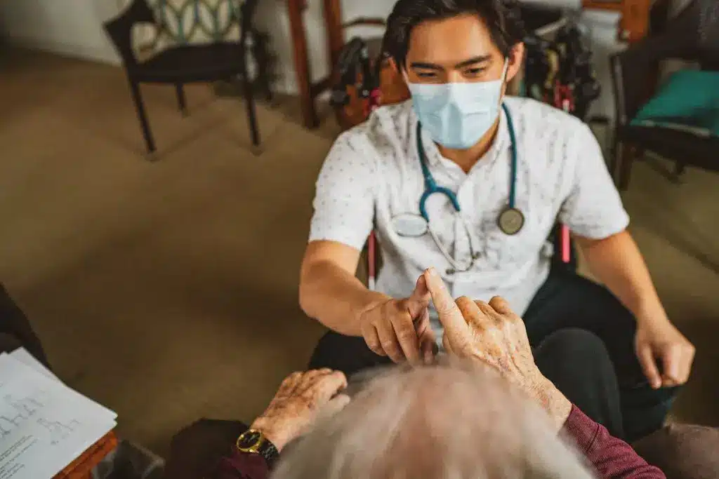 Doctor checking elderly patient's finger in home visit.