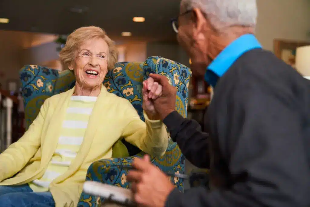 Elderly couple laughing and holding hands indoors.