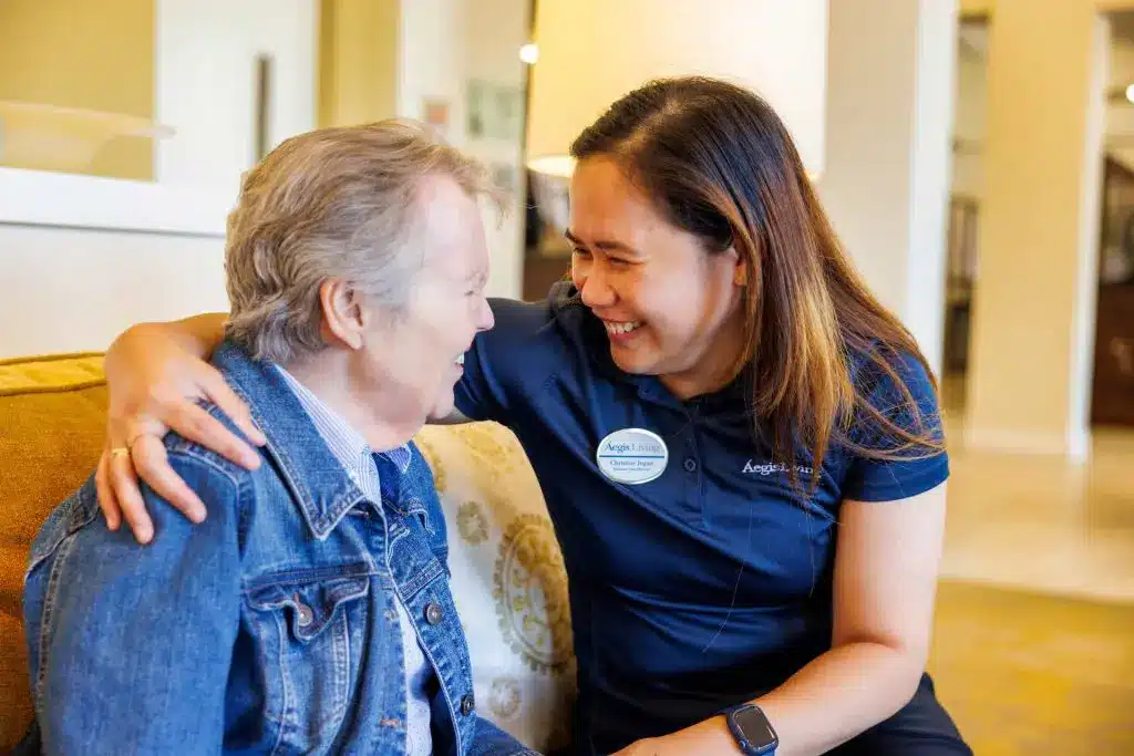 Caregiver smiling with elderly woman on couch.