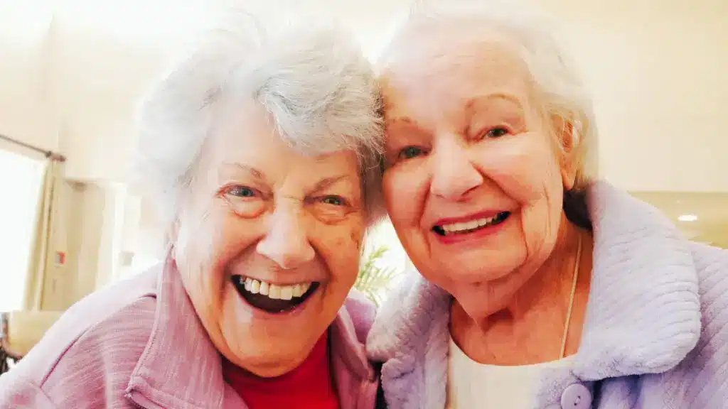 Two elderly women smiling together indoors.