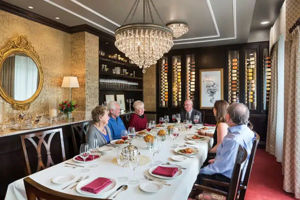 Group dining in elegant room with chandelier, wine display.