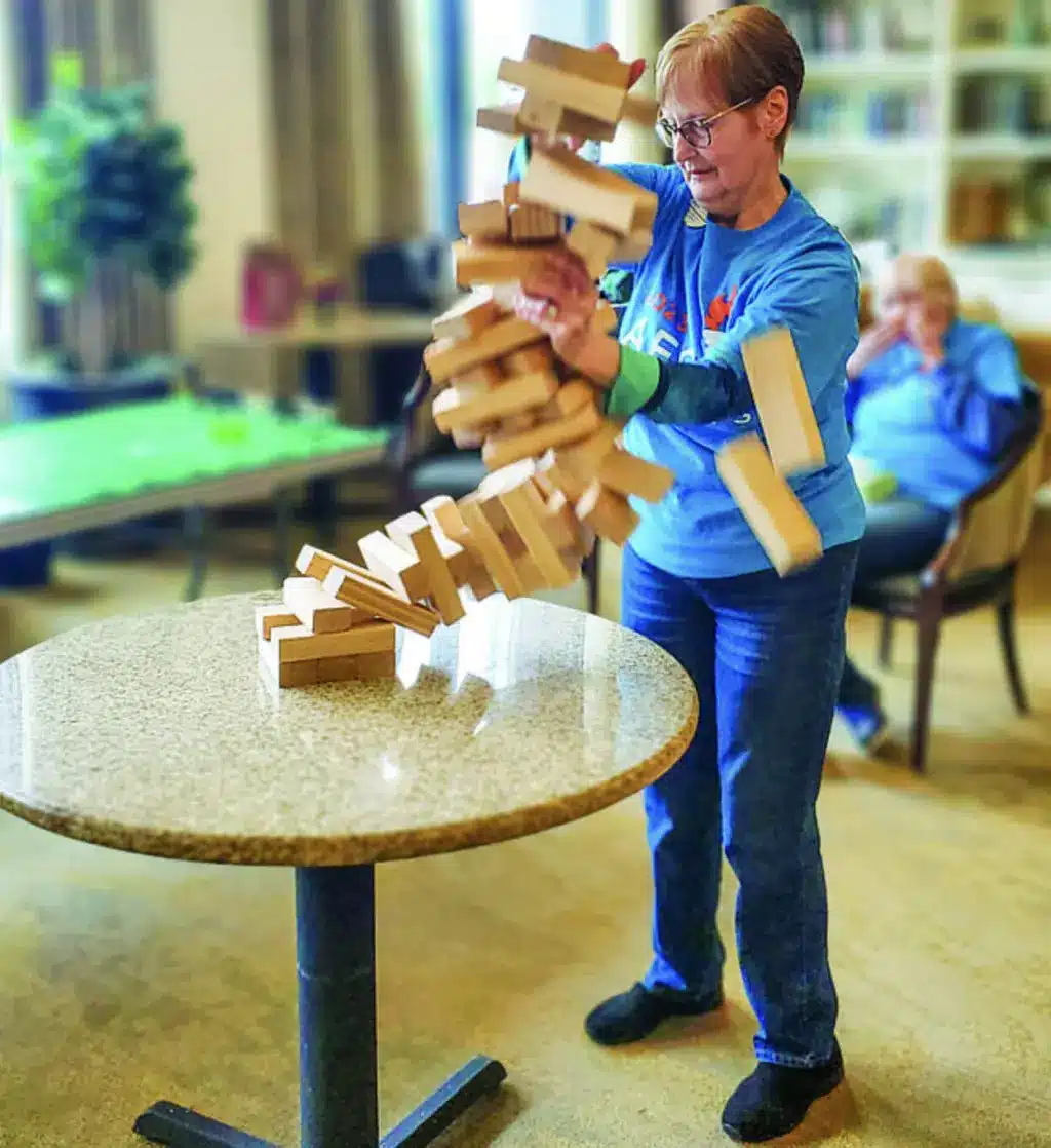 Woman playing with falling Jenga blocks on table.