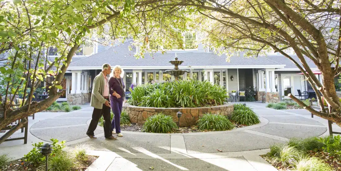 Elderly couple walking in garden courtyard.